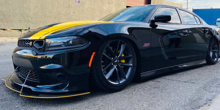 Black sedan with a distinctive yellow stripe on the hood, parked on a rough urban street. Crafted by a custom auto shop in Oakland County, MI, the car sits low to the ground with dark tinted windows and large black wheels.